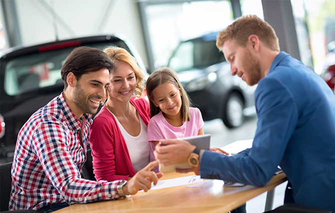 A happy couple with their child, speaking with a salesperson about benefits car finance
