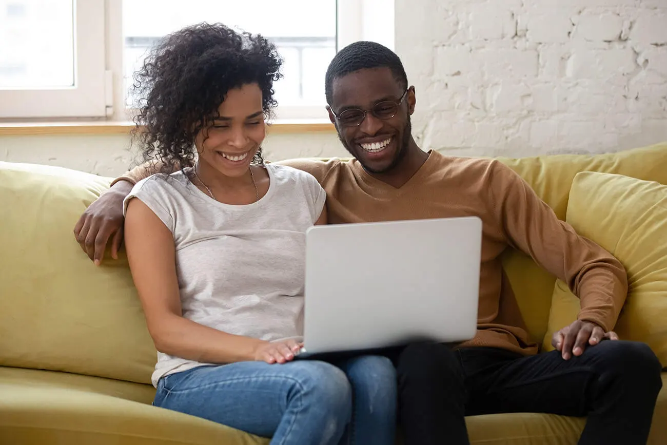 Happy couple on sofa with laptop after approval for Manchester car finance