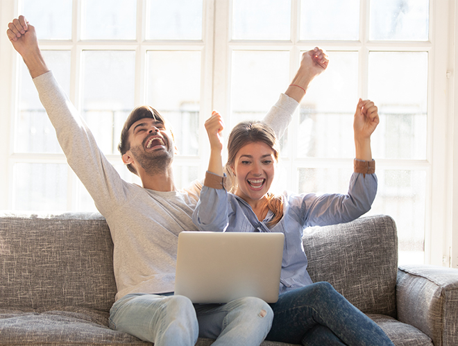 Happy couple with laptop celebrating on sofa no credit check car loans approval