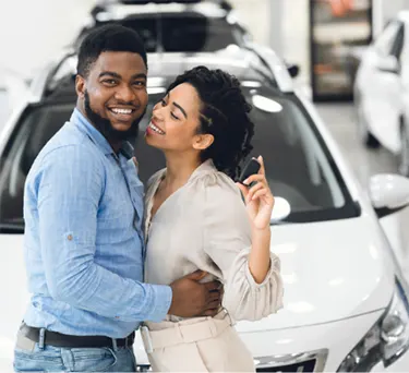 Happy couple standing in car showroom approved for a bad credit car loan